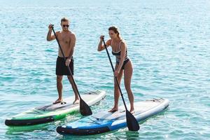 männliche und weibliche surfer, die standup-paddleboards im ozean reiten. foto