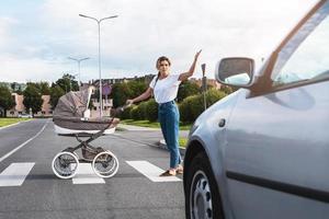 Empörte Mutter mit dem Kinderwagen, die mit einem Autofahrer auf dem Zebrastreifen in Konflikt gerät foto