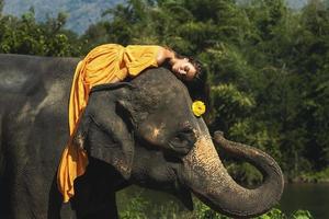 Frau, die ein schönes orangefarbenes Kleid trägt, reitet auf dem Elefanten foto