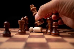 Nahaufnahme von Händen selbstbewusster Geschäftsmann, der Schachfigur im Wettbewerbserfolgsspiel bewegt. das schachspiel ist entwicklungsanalyse, strategie und plan, das management- oder führungskonzept.
