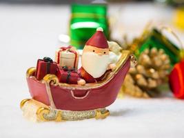 glücklicher weihnachtsmann mit geschenkbox auf dem schneeschlitten der hintergrund ist weihnachtsdekor. weihnachtsmann und weihnachtsdekor auf dem schnee. Konzept der frohen Weihnachten und des guten Rutsch ins neue Jahr foto