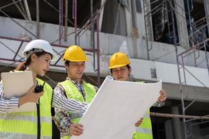 asiatische ingenieurin oder junge architektin setzen aus sicherheitsgründen einen helm auf und sprechen mit einem auftragnehmer über ein bauwerksprojekt, konzept der teamarbeit, führungskonzept. foto