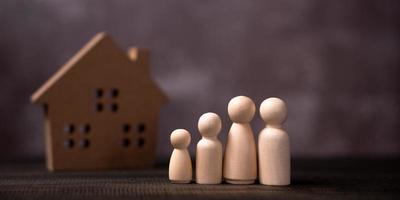 Holzfigurenfamilie steht vor einem Holzhaus. das konzept von schutz und sicherheit, haussicherheit, sachversicherung und haus. foto