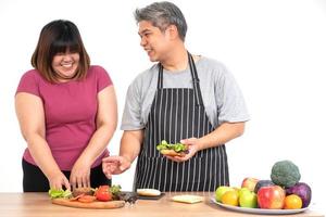glückliches übergewichtiges paar, das einen burger im küchenraum kocht. ein Gemüse auf dem Tisch. Konzept der glücklichen Familie und Binge Eating foto