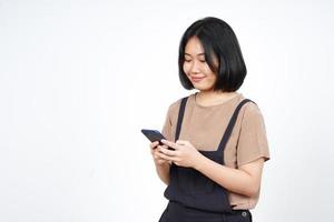 unter Verwendung des Smartphones und des Lächelns der schönen asiatischen Frau lokalisiert auf weißem Hintergrund foto