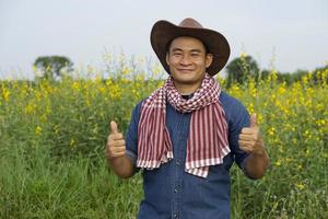 asiatischer Bauer trägt Hut, blaues Hemd, thailändischer Lendenschurz am Hals, Daumen hoch, fühlt sich sicher. konzept, landwirtschaftsberuf, zufrieden mit kulturen. foto
