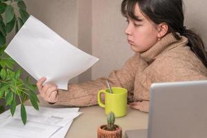 Mädchen arbeitet mit Dokumenten, die vor einem Laptop an ihrem Schreibtisch sitzen foto