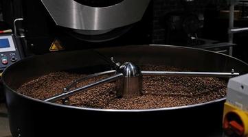 Kaffeeröstmaschine beim Kaffeerösten. Kaffeebohnen mischen. geröstete rotierende Kühler professionelle Maschinen und frische braune Kaffeebohnen Bewegung Nahaufnahme dunkles Foto im Werk.