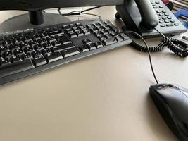 Schwarze, moderne Computermaus, Tastatur und Telefon auf einem funktionierenden Bürotisch in einem Unternehmen foto