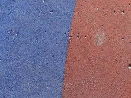 Blaue und rote Textur der weichen Gummioberfläche der sicheren Abdeckung des Sportspielplatzes für das Training aus gepresstem Feingummi. der Hintergrund. Textur foto
