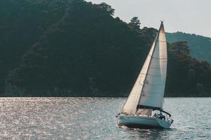 Segelyacht mit weißen Segeln in einer welligen Meeresbucht vor dem Hintergrund der Berge. foto