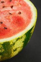 Hälfte der leckeren und reifen roten Wassermelone auf schwarzem Hintergrund, Textur aus saftigem Fruchtfleisch reifer roter Wassermelone mit Samen foto