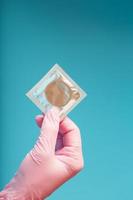 kondomverhütung eine hand in einem rosa handschuh hält eine kondompackung auf blauem hintergrund. foto