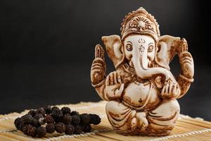 Hindu-Gott Ganesh auf schwarzem Hintergrund. Rudraksha-Statue und Rosenkranz auf einem Holztisch mit rotem Räucherstäbchen und Weihrauchrauch foto