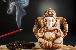 Ganesha auf schwarzem Hintergrund. Statue und Rosenkranz mit rot glimmendem Räucherstäbchen foto