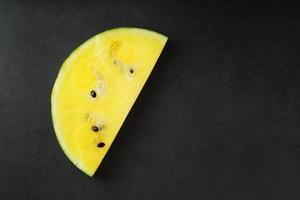 saftige Scheibe gelbe Wassermelone auf einem steinschwarzen Hintergrund. Konzeptfarben des Sommers. Draufsicht als Hintergrund oder Substrat foto