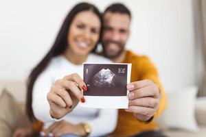 Frau und ihr Freund halten ein Bild ihres Sonogramms des Babys hoch. junges glückliches Paar mit Baby-Ultraschallfoto foto