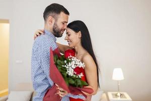 Valentinstag-Konzept. glückliches verliebtes Paar. Ein junges Liebespaar, das den Valentinstag feiert. Liebende umarmen sich. Schöner Mann überrascht seine Freundin zu Hause mit roten Rosen foto