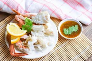 Krabbenfleisch - gekochte Krabbenkrallen und -beine auf weißem Teller und Meeresfrüchtesoße auf dem Tisch, blaue schwimmende Krabben foto