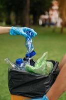 Die Hand der Frau nimmt Plastikabfälle zum Reinigen in den Recyclingbeutel zum Reinigen im Park. foto