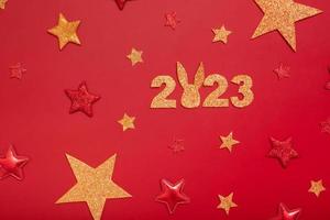 2023 Neujahrs-Flat-Lay-Konzept. zahlen 2023 mit roten und goldenen sternen und kaninchen, draufsicht auf rotem hintergrund foto