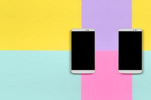 zwei moderne smartphones mit schwarzen bildschirmen auf texturhintergrund aus modepastellblauem, gelbem, violettem und rosafarbenem papier in minimalem konzept foto