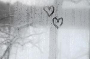 Zwei Herzen, die im Winter auf ein beschlagenes Glas gemalt wurden foto