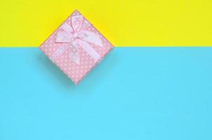 kleine rosa geschenkbox liegt auf texturhintergrund von modepastellblauem und gelbem papier in minimalem konzept foto