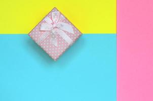 kleine rosa geschenkbox liegen auf texturhintergrund von modepastellblauem, gelbem und rosafarbenem papier in minimalem konzept foto