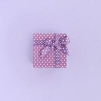 kleine lila geschenkbox mit band liegt auf violettem hintergrund. minimalismus flach draufsicht foto