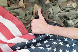 Hand zeigt Daumen nach oben auf amerikanische Flagge und Militäruniform foto