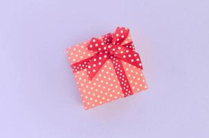 kleine rote geschenkbox mit band liegt auf violettem hintergrund. minimalismus flach draufsicht foto