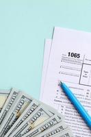 1065 Steuerformular liegt in der Nähe von Hundert-Dollar-Scheinen und blauem Stift auf hellblauem Hintergrund. uns für Elternschaftseinkommen zurückgeben foto