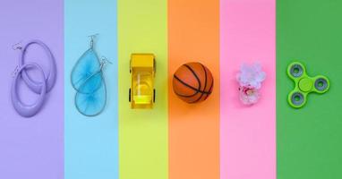 trendige, modische Pastellkomposition mit Ohrringen, Sonnenbrille, Getränkedose, Basketballball, Spielzeuglastwagen, Blume und Spinner auf rosa, violettem, grünem, orangefarbenem, gelbem und blauem Hintergrund foto