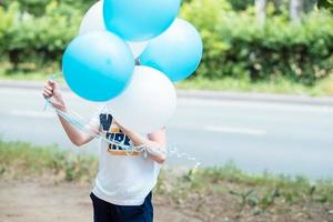 der junge bedeckt sein gesicht mit blauen luftballons auf der straße. Geburtstagsparty foto