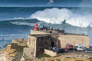 nazare, portugal - 7. november 2022 leute beobachten die großen riesigen wellen, die in der nähe des forts des leuchtturms von nazare in nazare, portugal, zusammenbrechen. größten wellen der welt. touristisches Ziel zum Surfen.