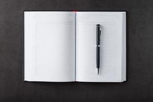 Schreibtisch mit einem schwarzen offenen Notizbuch und einem Stift auf schwarzem Hintergrund. foto