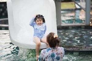 asiatische mutter und tochter schwimmen, spielen rutschenpool im pool des resorts, lächeln und lachen. spaß im pool des resorthotels, familienfreundliches konzept. foto