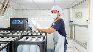 junger mannarbeiter oder qualitätsinspektor in arbeitskleidung und mit einer schutzmaske im gesicht, der vor dem versand abgefülltes trinkwasser in der trinkwasserfabrik überprüft. trinkwassergeschäft foto