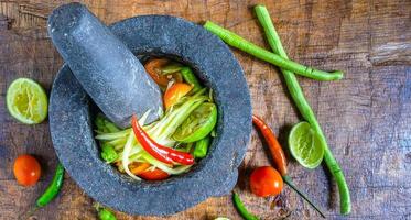 kochen des menüs thailändisches essen papayasalat mit zitrone und tomate auf einem hölzernen hintergrund.draufsicht foto