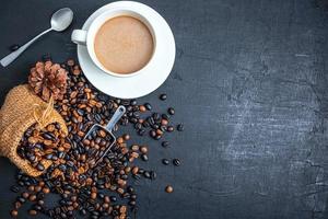 Draufsicht auf eine Mischung aus dunkler Röstung und mittlerer Röstung gerösteter Kaffeebohnen in einem braunen Sackbeutel mit heißer Kaffeetasse foto