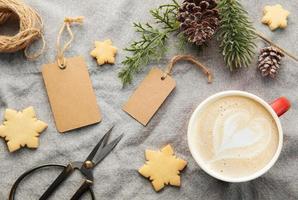 leere geschenkanhänger mit tannenzweig, tasse kaffee und weihnachtsplätzchen auf textilhintergrund. das konzept der vorbereitung auf die weihnachtsferien foto
