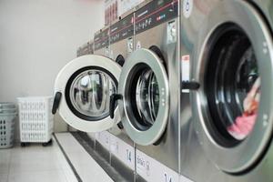 Selektiver Fokus auf die Vordertür der Waschmaschine mit verschwommenen Türen im Vordergrund. Reihe von Waschmaschinen in der Waschküche foto