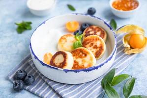 Käsepfannkuchen, Krapfen oder Syrniki mit Blaubeere, Physalis und Joghurt, blauer Hintergrund. Gesundes und leckeres Frühstück. foto