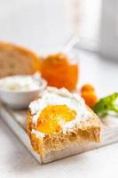 In Scheiben geschnittenes hausgemachtes Brot mit Ricotta oder Hüttenkäse und Orangenmarmelade auf hellem Hintergrund. leckeres Frühstück. High-Key-Fotografie. foto