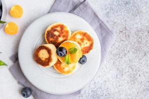 Hüttenkäsepfannkuchen, süße Quarkkrapfen mit Blaubeere und Physalis, konkreter Hintergrund. Syrniki mit Marmelade und Beeren für ein gesundes Frühstück. foto