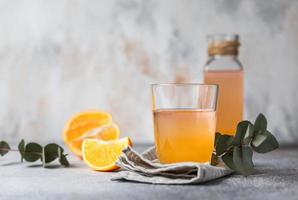 orangenlimonade in glas und flasche mit frischem orangefarbenem, konkretem hintergrund. erfrischendes Getränk. Cocktailbar-Hintergrundkonzept.