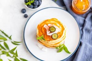 Stapel flauschiger Pfannkuchen mit Orangenmarmelade, Heidelbeeren, Kokoschips und Minze, heller Hintergrund. traditionelles Frühstück. High-Key-Fotografie. foto