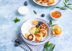 Käsepfannkuchen, Krapfen oder Syrniki mit Blaubeere, Physalis und Joghurt, blauer Hintergrund. Gesundes und leckeres Frühstück. foto