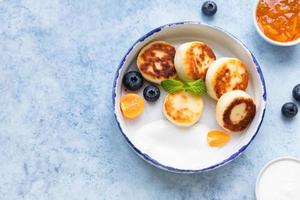 Käsepfannkuchen, Krapfen oder Syrniki mit Blaubeere, Physalis und Joghurt, blauer Hintergrund. Gesundes und leckeres Frühstück. foto